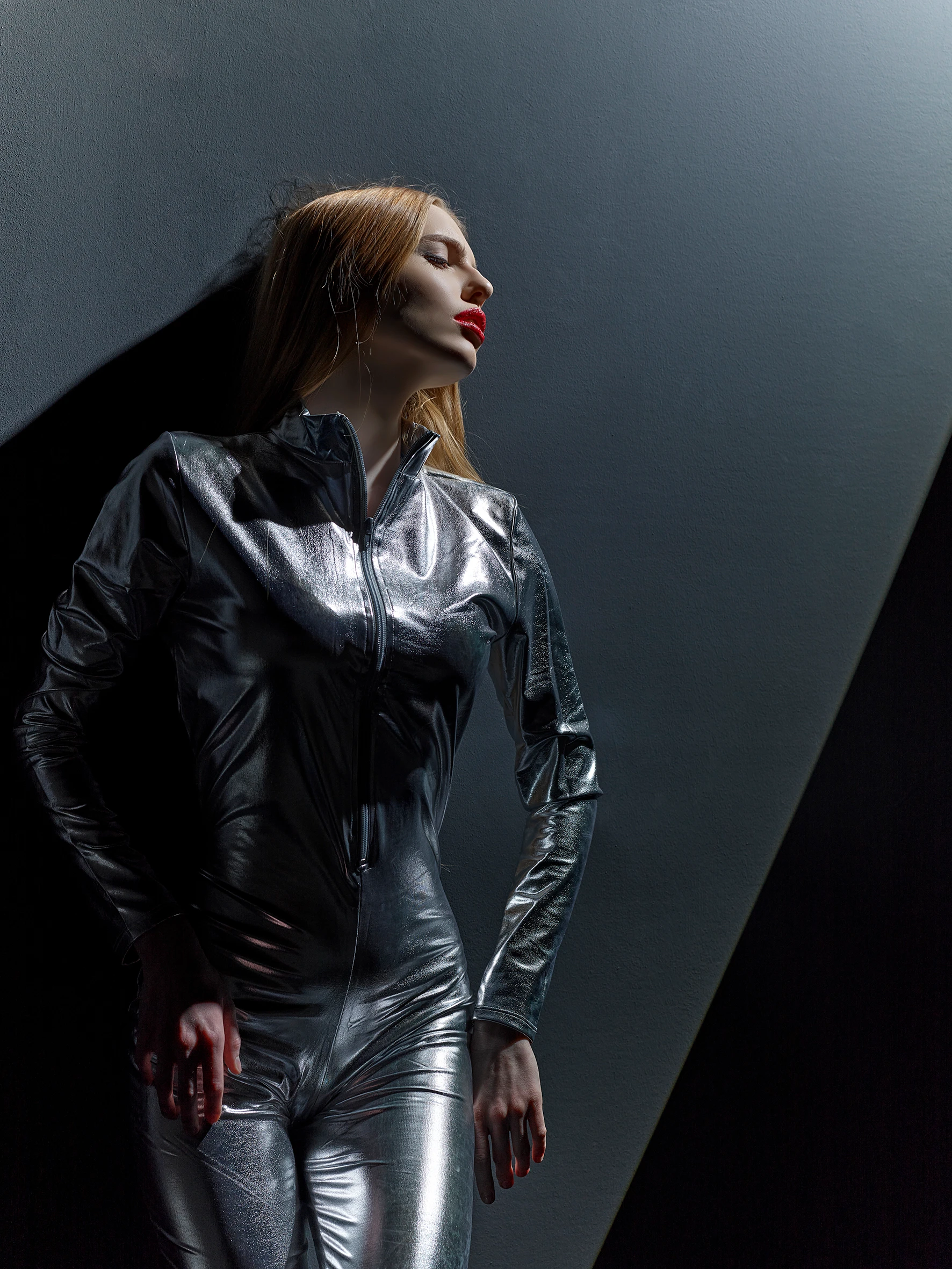 girl in a full silver suit standing under spotlight laying to the wall