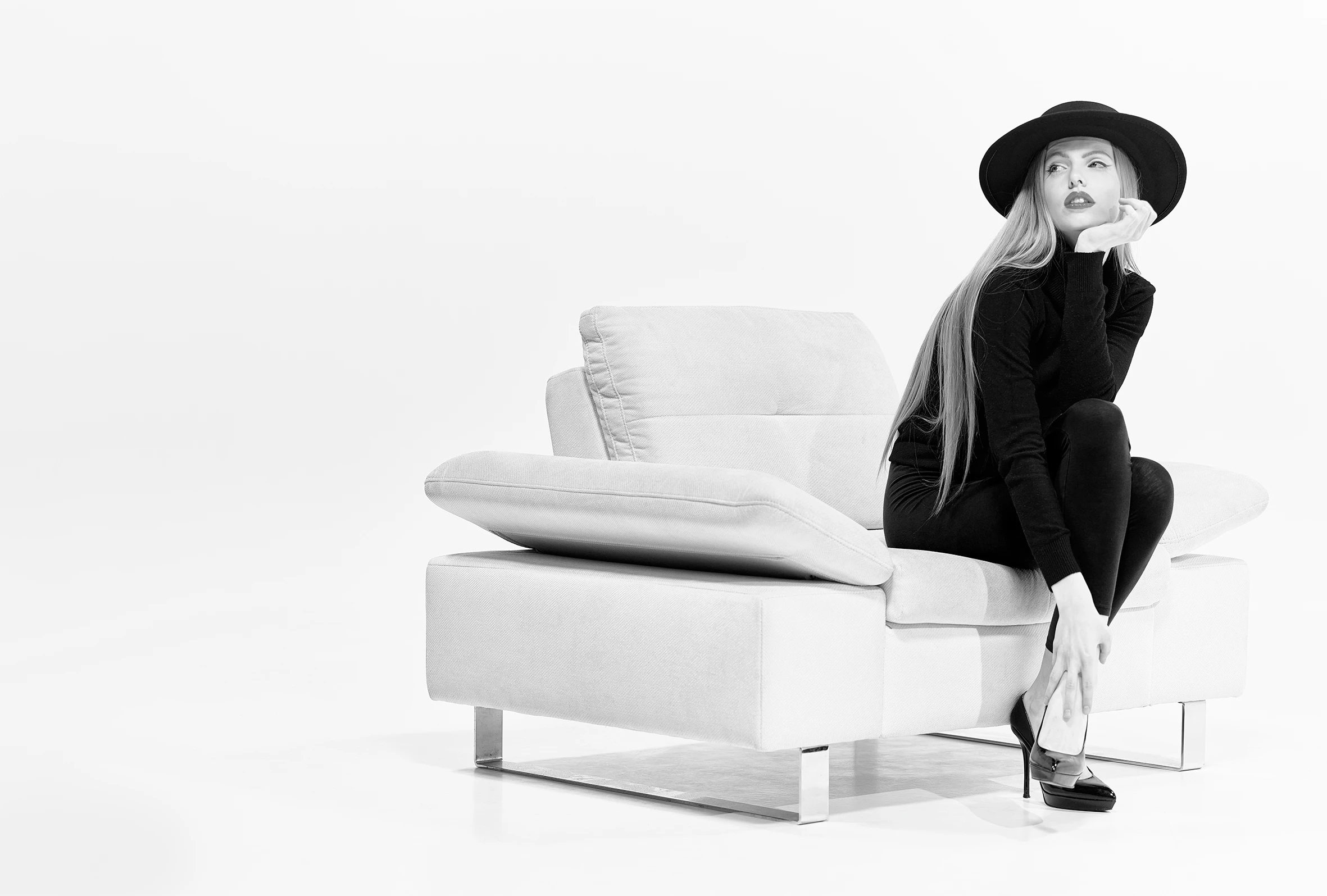 A monochrome image of a young girl with a hat sitting on a sofa